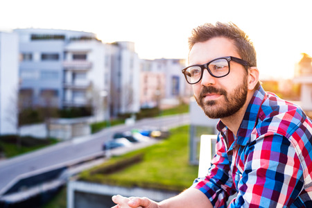 Young hipster businessman in checked shirt standing on a balcony, relaxingの写真素材