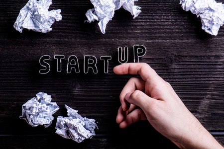 Office desk with start up sign made of cookie cutters and hand of unrecognizable man. Crumpled paper balls. Flat lay. Workplace. Studio shot on wooden background.の写真素材