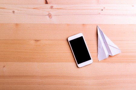 Paper airplane and smart phone against wooden background, empty copy space