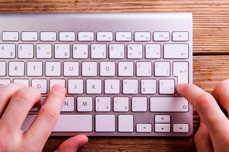 Hands of unrecognizable man working on computer keyboard laid on an old office desk. Studio shot on...