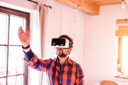 Young man wearing virtual reality goggles standing in a kitchen