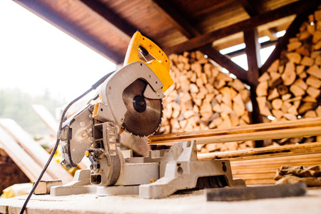 Close up of circular saw laid on table, stack of wood behind it