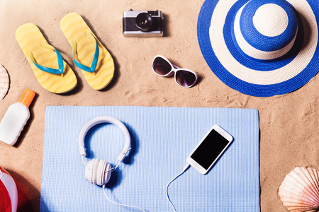 Summer vacation composition with a pair of yellow flip flop sandals, hat, sunglasses, sun cream and other stuff on a beach. Sand background, studio shot, flat lay.の写真素材