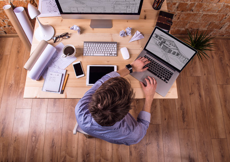 Businessman at the desk, wearing smart watch, working on laptop. Computer, tablet, smart phone and various office supplies around the workplace.の写真素材