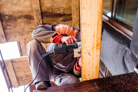 Carpenter with grinder. Man grinding planks of wood for home construction.
