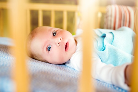 Close up cute little baby boy lying in wooden cribの写真素材