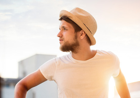 Handsome hipster man in white t-shirt and hat on beach. Enjoying time at seaside. Sunsetの写真素材