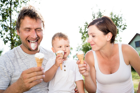 Young parents with their little son eating ice cream, sunny summer gardenの写真素材