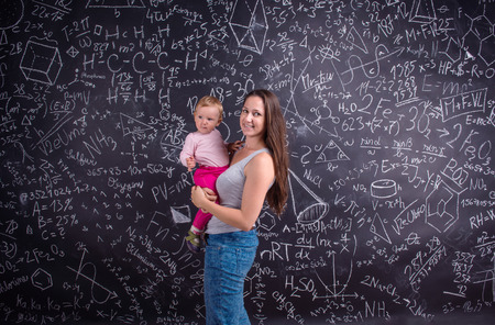 Beautiful young mother with little daughter against big blackboard with formulas and mathematical symbolsの写真素材