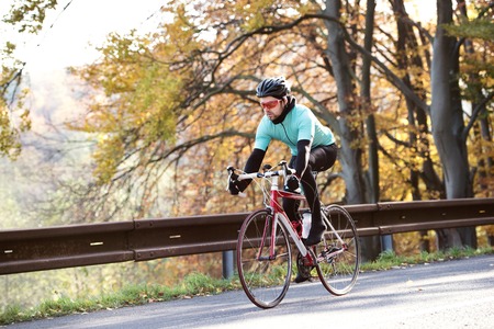 Young handsome sportsman riding his bicycle outside in sunny autumn natureの写真素材