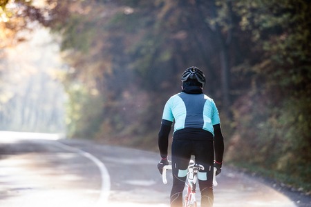 Young handsome sportsman riding his bicycle outside in sunny autumn nature, rear viewの写真素材