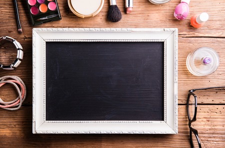 White picture frame with black board in it and various make up products laid on table. Studio shot on wooden background. Flat lay, copy space.の写真素材