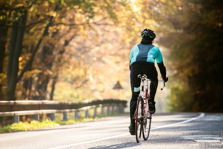 Young handsome sportsman riding his bicycle outside in sunny autumn nature, rear viewの写真素材