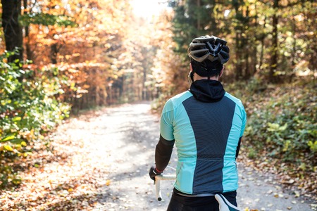 Young handsome sportsman riding his bicycle outside in sunny autumn nature, earphones in his ears, rear viewの写真素材
