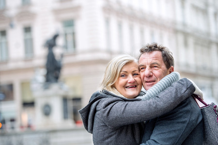 Beautiful senior couple on a walk, hugging in historical centre of the city of Vienna, Austria. Woman holding handbag in her hand. Winter.の写真素材