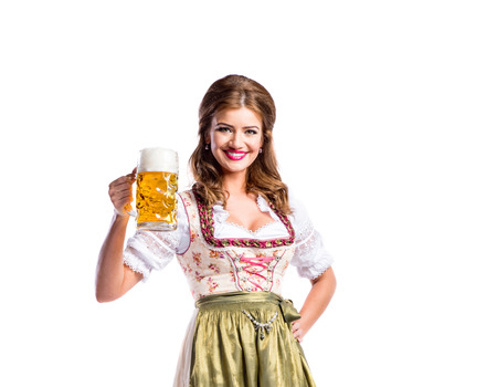 Beautiful young woman in traditional bavarian dress holding a mug of beer. Oktoberfest. Studio shot on white background, isolated.の写真素材