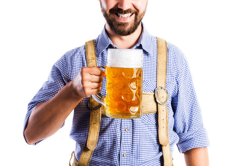 Unrecognizable young man in traditional bavarian clothes holding a mug of beer. Oktoberfest. Studio shot on white background, isolated.の写真素材