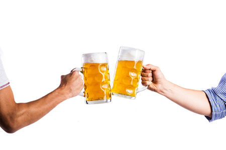 Hands of two unrecognizable men clinking with beer mugs. Oktoberfest. Studio shot on white background, isolated.の写真素材