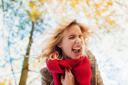 Beautiful young woman in checked coat and red knitted scarf in autumn park laughing and shouting