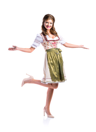 Beautiful young woman in traditional bavarian dress standing. Oktoberfest. Studio shot on white background, isolated.の写真素材