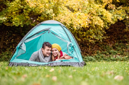 Beautiful young couple lying in tent, camping in autumn natureの写真素材