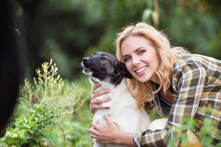 Beautiful blond woman with her dog in green gardenの写真素材