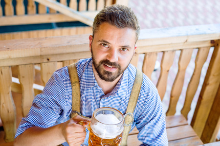 Man in traditional bavarian clothes sitting at the table with mug of beer. Pretzels in wicker basket. Oktoberfest.の写真素材