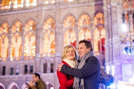 Senior couple in winter clothes on a walk in illuminated night city. Historical building. Vienna, Austria.の写真素材