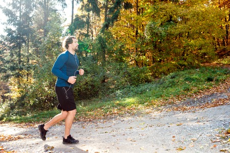 Young handsome runner with earphones in his ears, listening music, outside in sunny autumn natureの写真素材