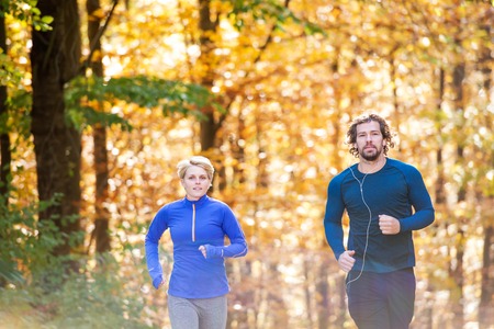 Beautiful couple running together outside in sunny autumn forestの写真素材