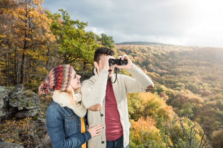 Beautiful young couple on a walk in sunny autumn forest, man looking through binocularsの写真素材