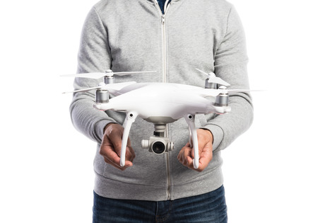 Unrecognizable man in gray sweatshirt holding drone with camera. Studio shot on white background,...