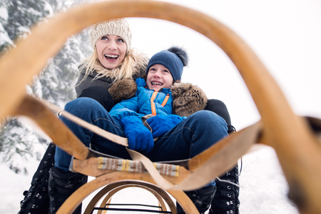 Beautiful young mother with her son on sledge, foggy white winter nature. Close up.の写真素材