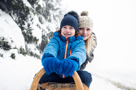Beautiful young mother with her son on sledge, foggy white winter nature. Close up.の写真素材