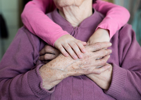 Close up. Unrecognizable granddaughter holding hands of her grandmother. Studio shot on white wooden...