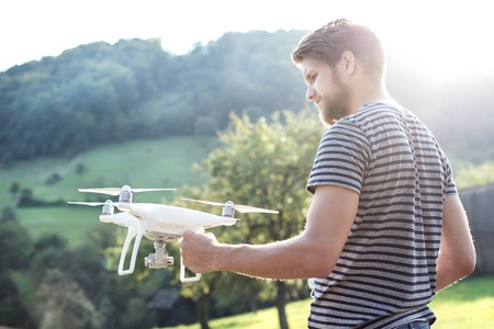Young hipster man holding drone with camera. Green sunny nature. Rear view.