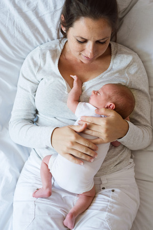 Beautiful young mother with her newborn baby son, lying in bed in bedroomの写真素材