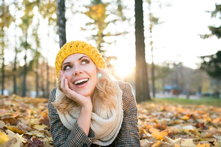 Beautiful young woman in checked coat and knitted scarf and hat in autumn park lying on the groundの写真素材