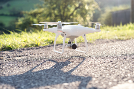 Flying helicopter drone with rised landing gears and camera, landing or taking off. Country road,...