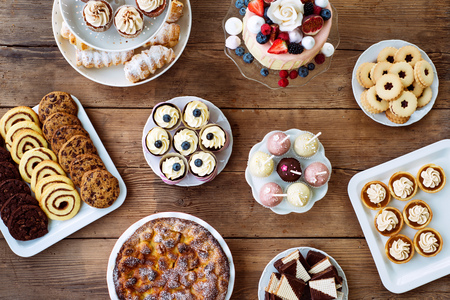 Table with cake, pie, cupcakes, cookies, tarts and cakepops. Studio shot on brown wooden background. Flat lay.の写真素材