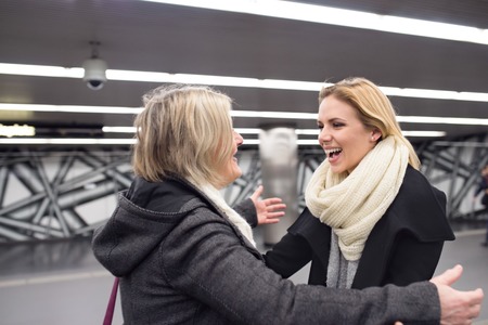 Two beautiful women, mother and daughter, standing at the underground platform, hugging. Welcoming or saying good bye.の写真素材