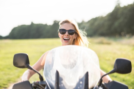 Pretty blond woman enjoying a quad bike ride in countryside. Girl driving off-road with ATV.の写真素材
