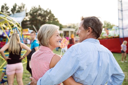 Senior couple having a good time at the fun fair, hugging. Woman holding lollipop. Rear view.の写真素材