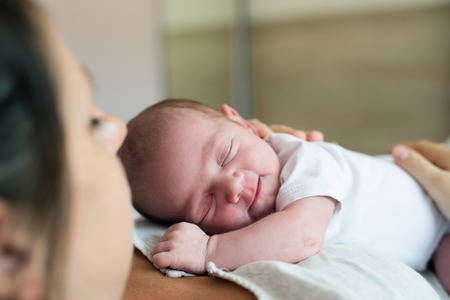 Unrecognizable young mother lying in bed in bedroom with her sleeping newborn baby son