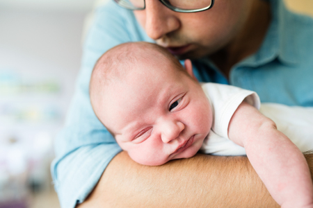 Close up, unrecognizable father holding his newborn baby son in his arms, kissing himの写真素材