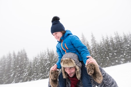 Young father outside giving his son piggyback. Having fun with his son, playing in the snow. Foggy white winter nature.の写真素材