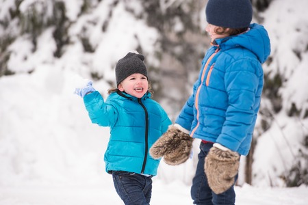 Two cute boys in blue jackets, hats and gloves playing outside in winter nature, throwing snow ballsの写真素材