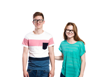 Teenage couple wearing eyeglasses, smiling. Young woman in green t-shirt holdidng man in striped t-shirt. Studio shot on white background, isolated.の写真素材