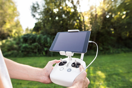 Unrecognizable young man with remote control and tablet. Green sunny nature.