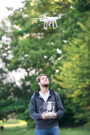 Young hipster man with remote control and flying drone with camera. Green sunny nature.
